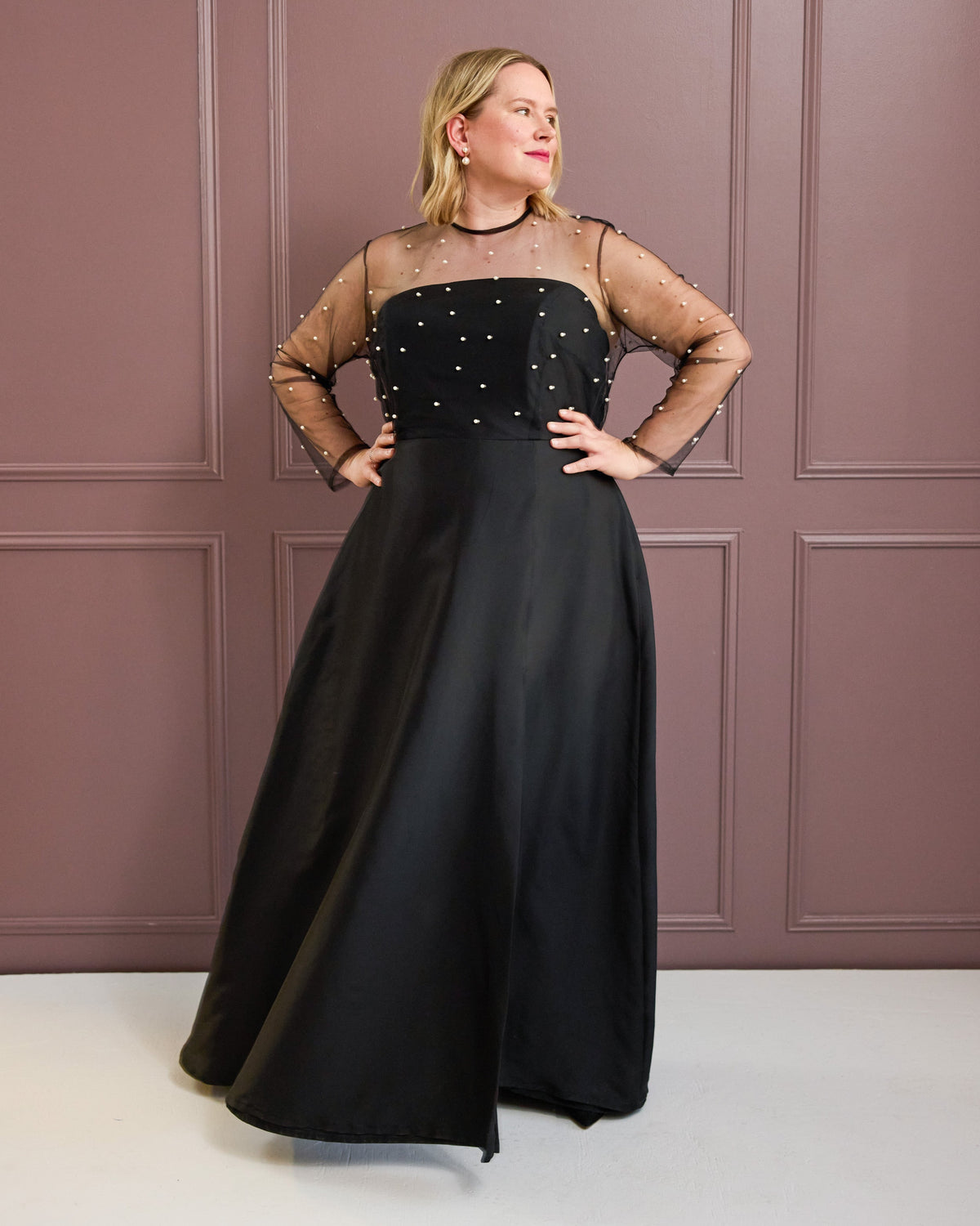 Cashmerette Ellington Dress PDF sewing pattern, woman wearing a black evening gown with sheer sleeves against a pink paneled wall, black version
