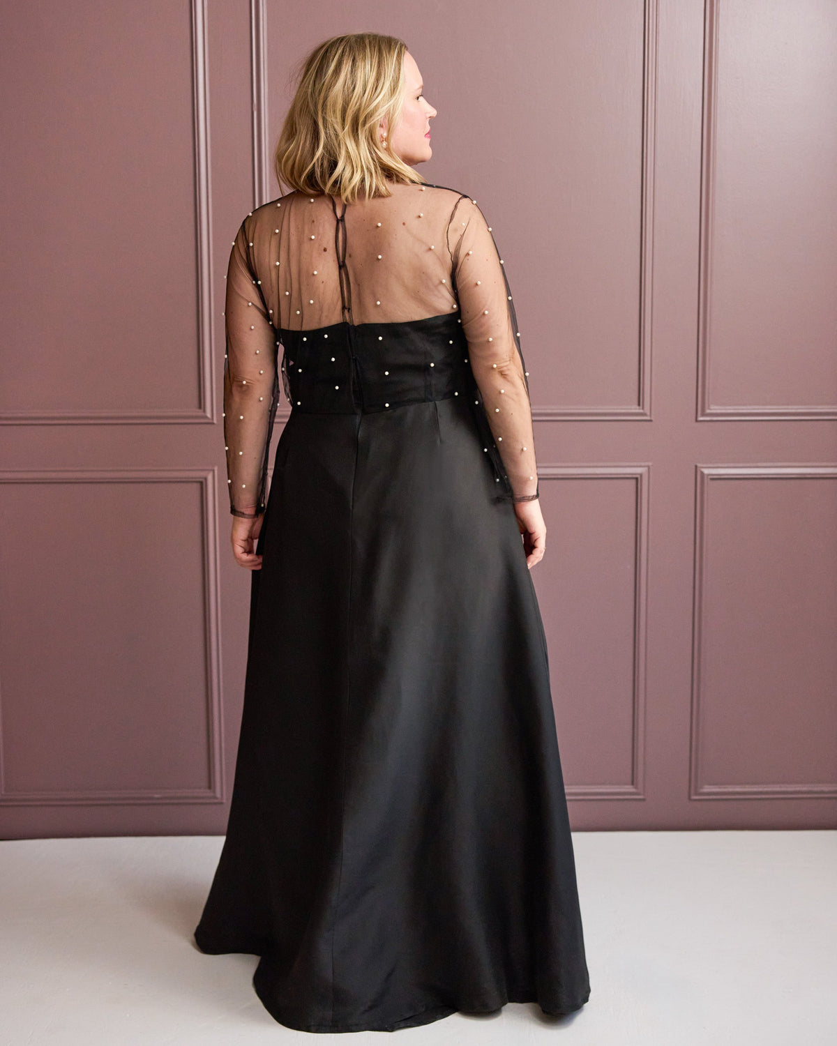 Cashmerette Ellington Dress PDF sewing pattern, woman wearing a black evening gown with sheer sleeves against a pink paneled wall, front view