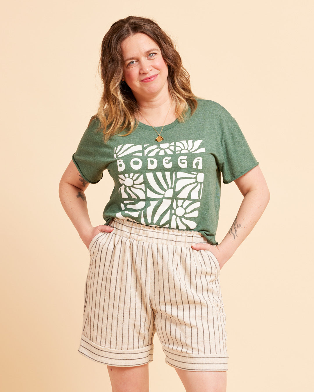 Cashmerette Everett Pants and Shorts PDF sewing pattern, woman wearing a green t-shirt with 'BODEGA' print and beige shorts