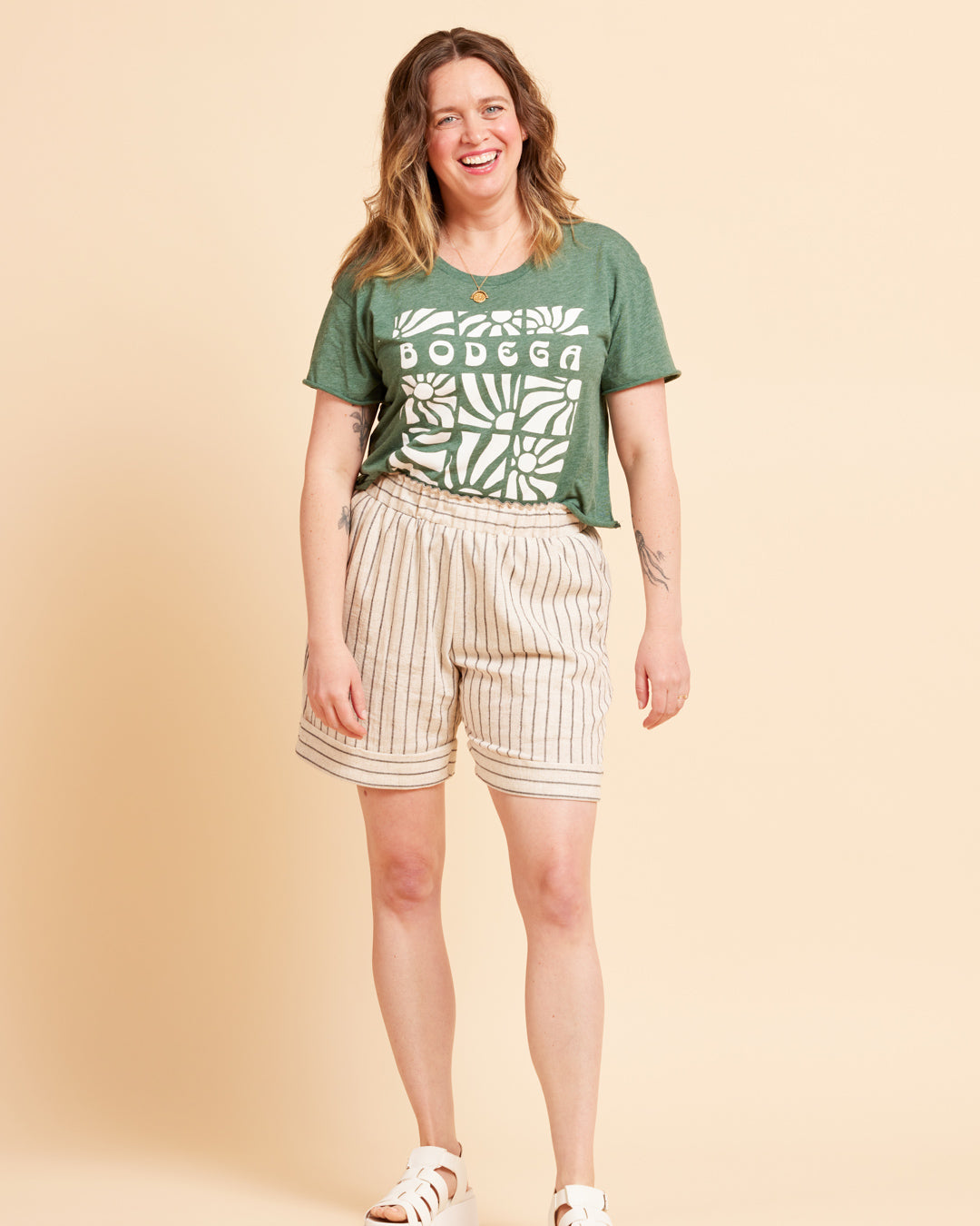Cashmerette Everett Pants and Shorts PDF sewing pattern, woman wearing a green t-shirt with 'Bodega' print and beige shorts