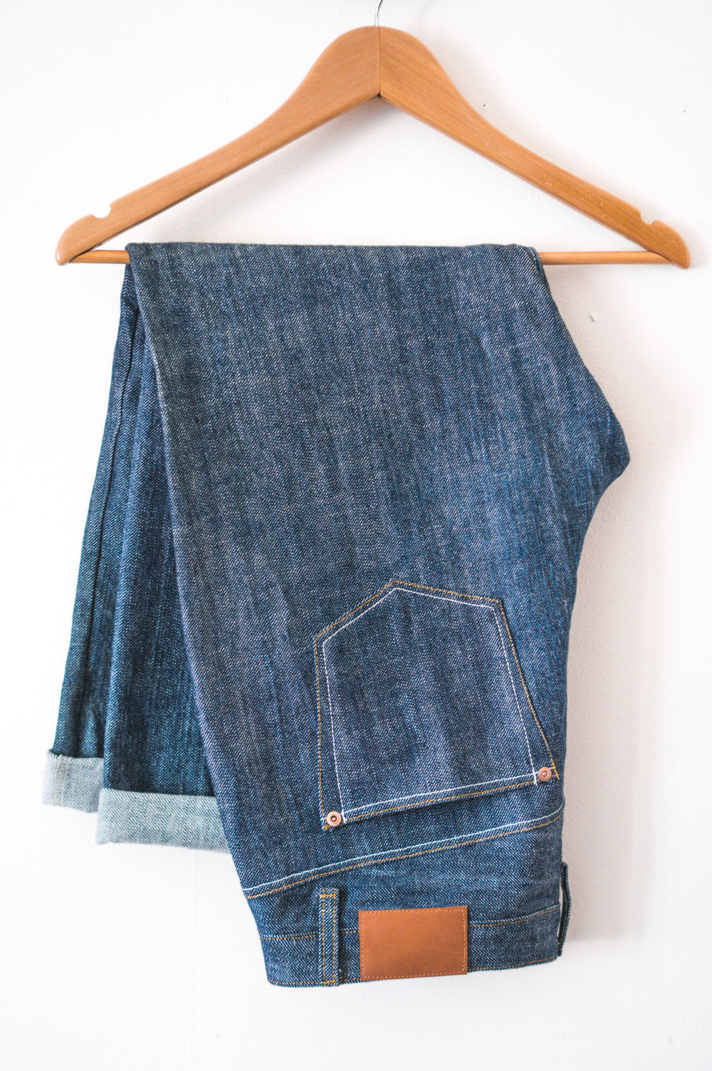 Folded denim jeans sewn from the Closet Core Morgan Boyfriend Jeans PDF sewing pattern on a wooden hanger