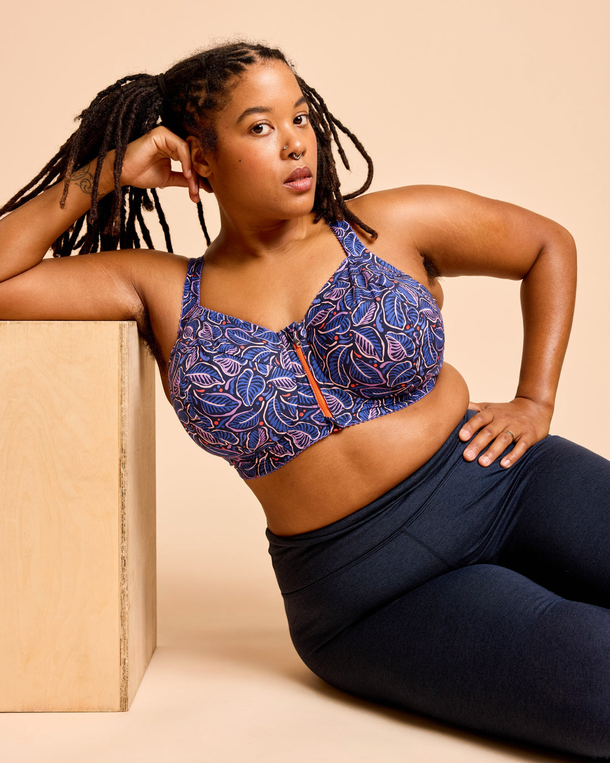 Cashmerette Somerville Sports Bra PDF sewing pattern, woman wearing a blue patterned sports bra and navy leggings, seated