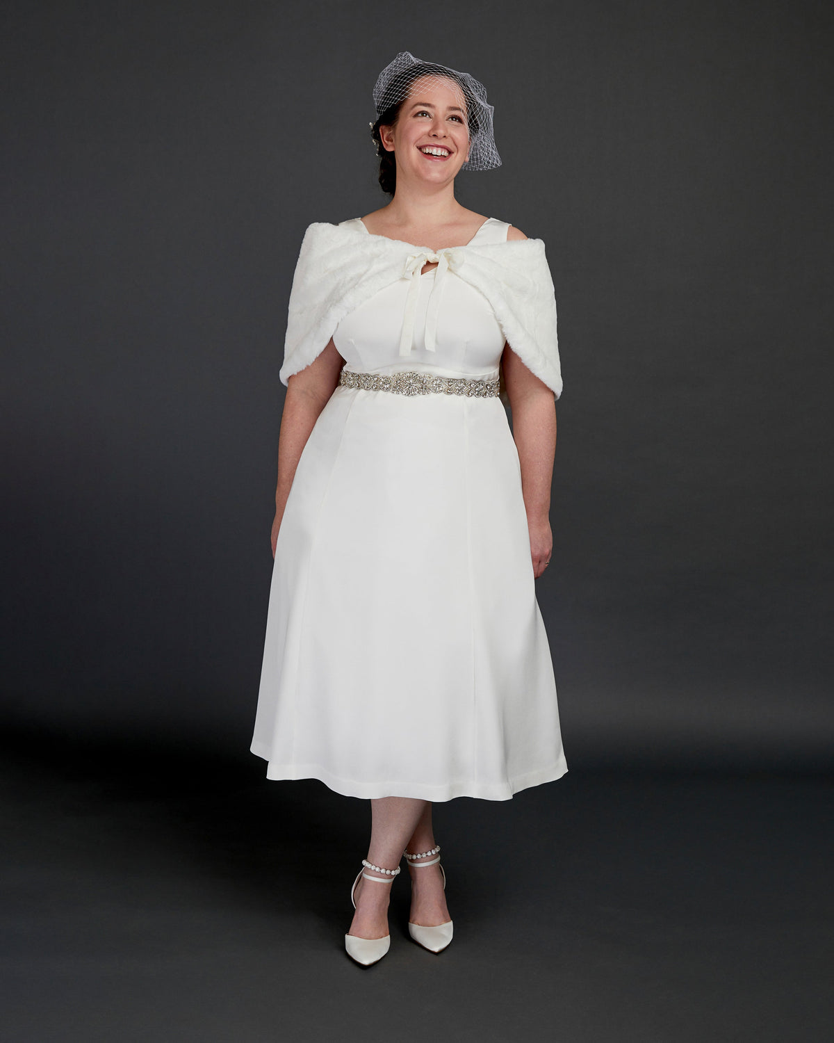 Cashmerette Upton Dress and Skirt Plus expansion pack PDF sewing pattern, woman wearing a white dress with a fur shrug and hat against a dark