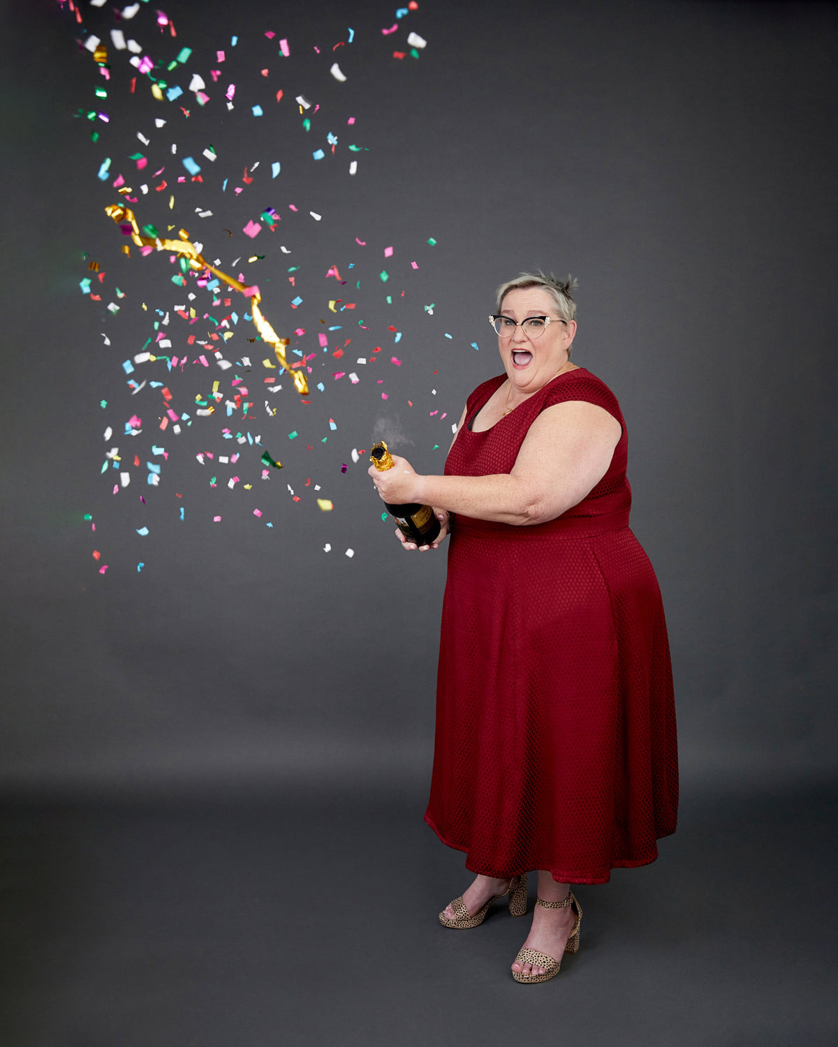 Cashmerette Upton Dress and Skirt Plus expansion pack PDF sewing pattern, woman in a red dress holding a bottle with confetti falling around her on a