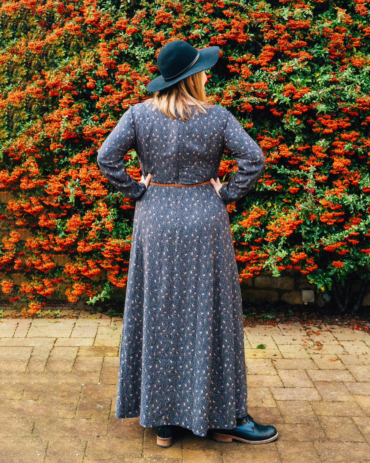Cashmerette Upton Dress and Skirt Plus expansion pack PDF sewing pattern, woman in a long dark dress and black hat standing in front of a wall of