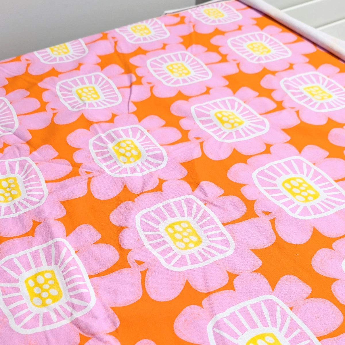 Riku Flower in Apricot printed fabric laid flat, pink flowers on apricot orange